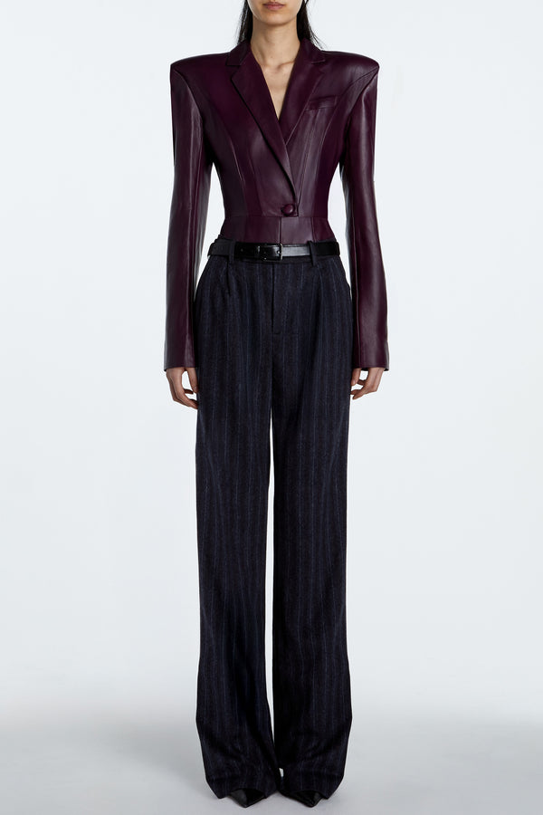 Model wearing aubergine leather tailored bodysuit with structured shoulder silhouette and high-waisted trousers.