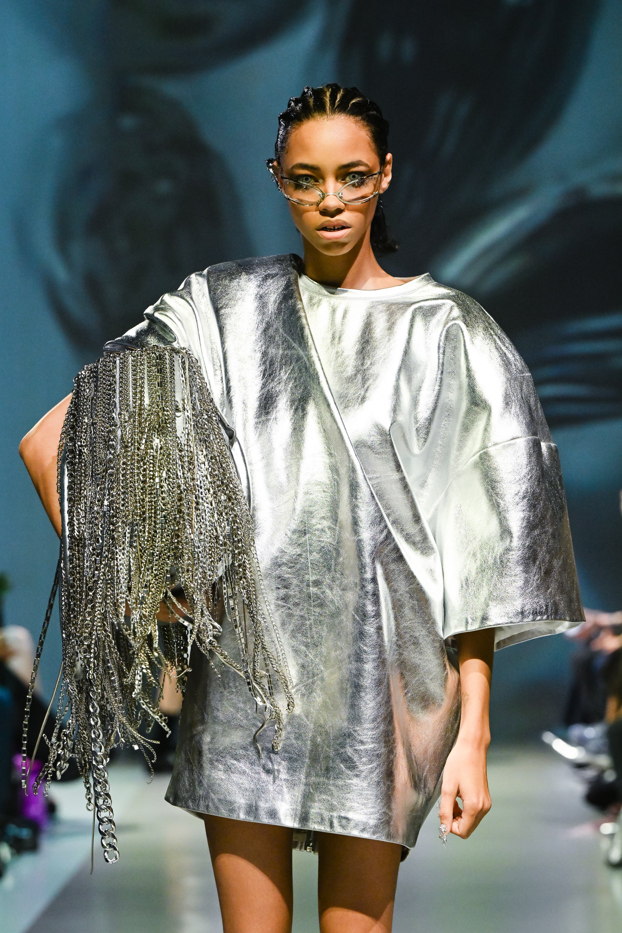 Model wearing the Silver Metallic Leather Mini Dress with a loose sculptural silhouette, featuring shiny reflective leather and an oversized fringe chain accessory, showcasing SHAO New York bespoke tailoring.