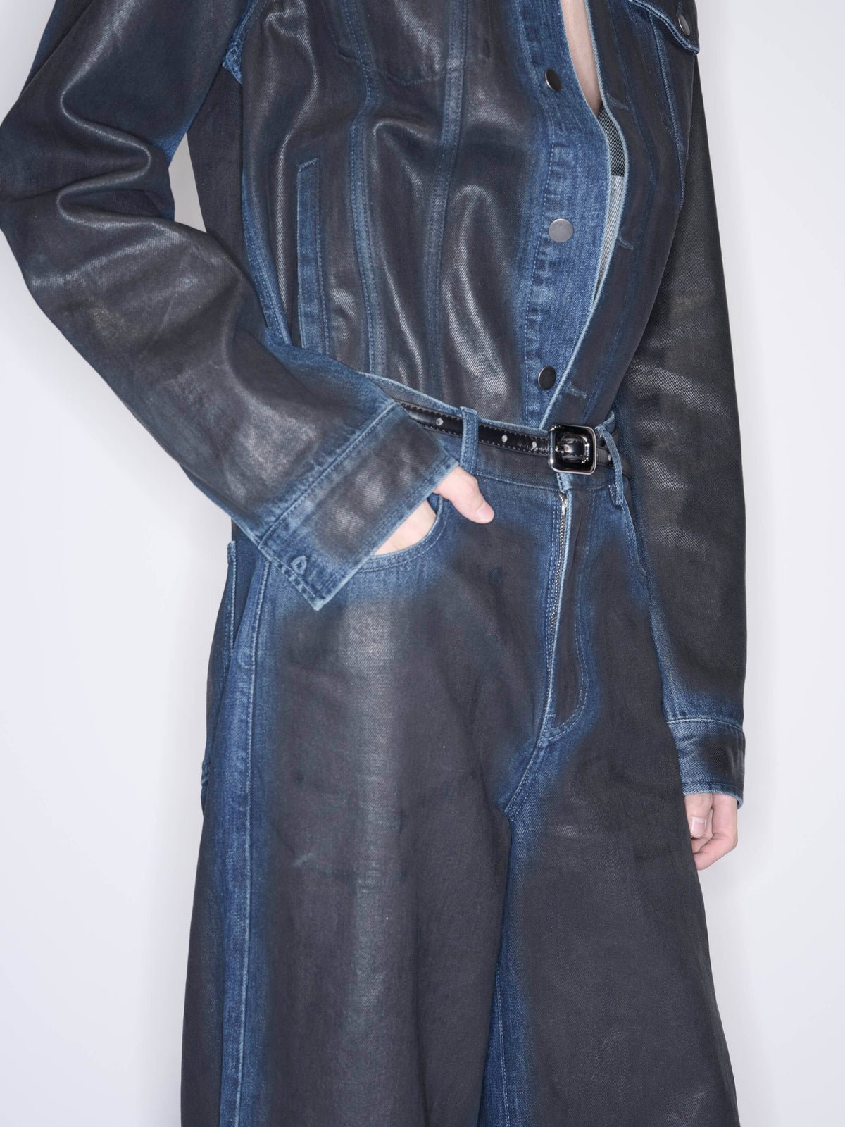 A person wearing a dark denim jumpsuit with a black belt, shown from the chest down against a plain light background.